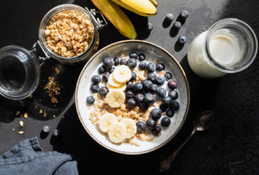 Healthy breakfast oat cereals with milk, blueberry and banana on black concrete backdrop. Table top view, harsh light food photography
