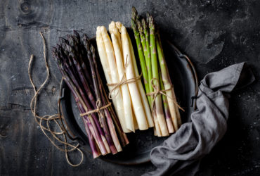 Bunches of fresh green, purple, white asparagus on vintage metal tray over dark grey rustic background. Top view, copy space